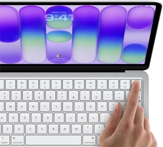 MacBook Neo, silver color, showing login screen, person's finger on Touch ID sensor in top-right corner of keyboard