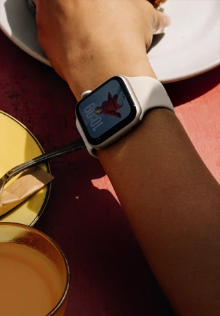 ذراع شخص يتناول الفطور وعلى معصمه Apple&nbsp;Watch&nbsp;SE&nbsp;3‏ بإطار من الألومنيوم ولون ضوء النجوم، وشاشة بميزة "التشغيل دوماً"، وواجهة الساعة تحمل صورة بورتريه، وحزام رياضي بلون ضوء النجوم